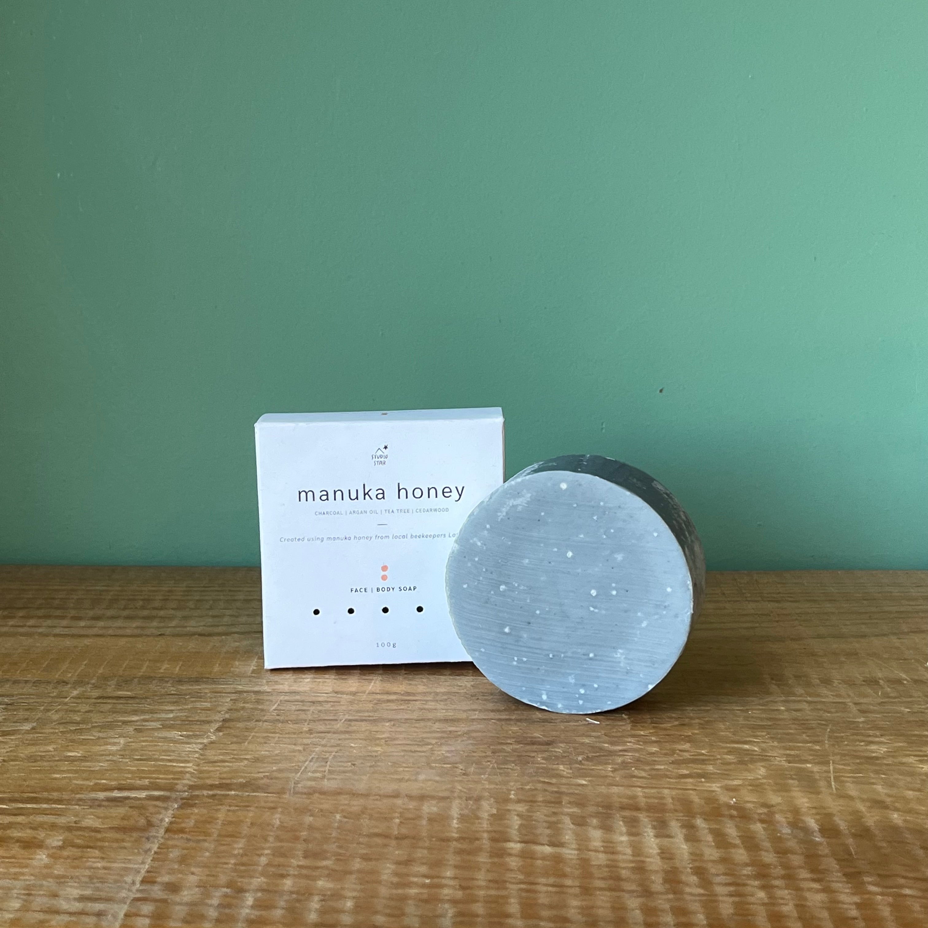 Manuka honey product and packaging on a wooden surface with a green background